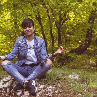 A woman meditates peacefully in a lush green forest, exuding calm and relaxation.