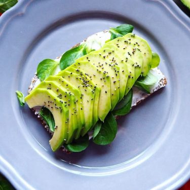 Delicious avocado toast with chia seeds and fresh tomatoes on a grey plate.
